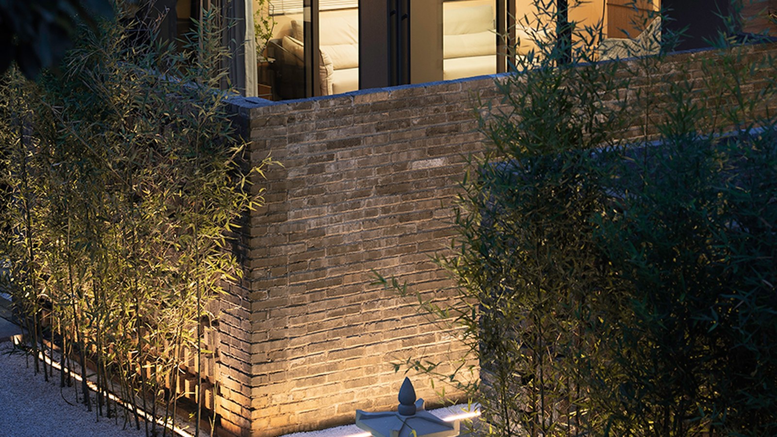 Brick retaining wall in a courtyard, uplighted by an outdoor wall washer